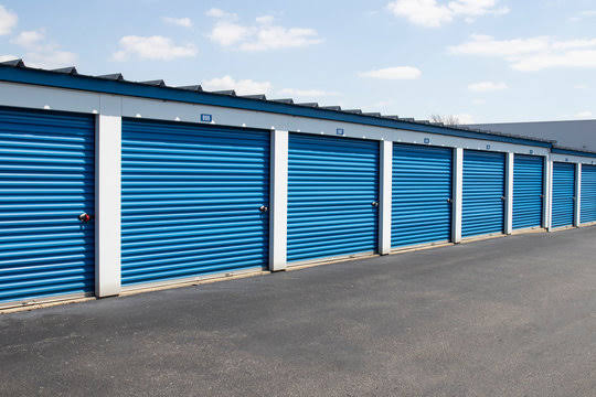 A row of blue roll-up storage unit doors along a paved drive aisle